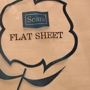 K&ouml;nnte beinhalten: Ein flaches Bettlaken in einer transparenten Plastikverpackung. Die Verpackung zeigt ein blau-wei&szlig;es Sears-Logo und die Worte "FLAT SHEET" in schwarzer Schrift. Das Laken scheint eine helle Farbe zu haben.