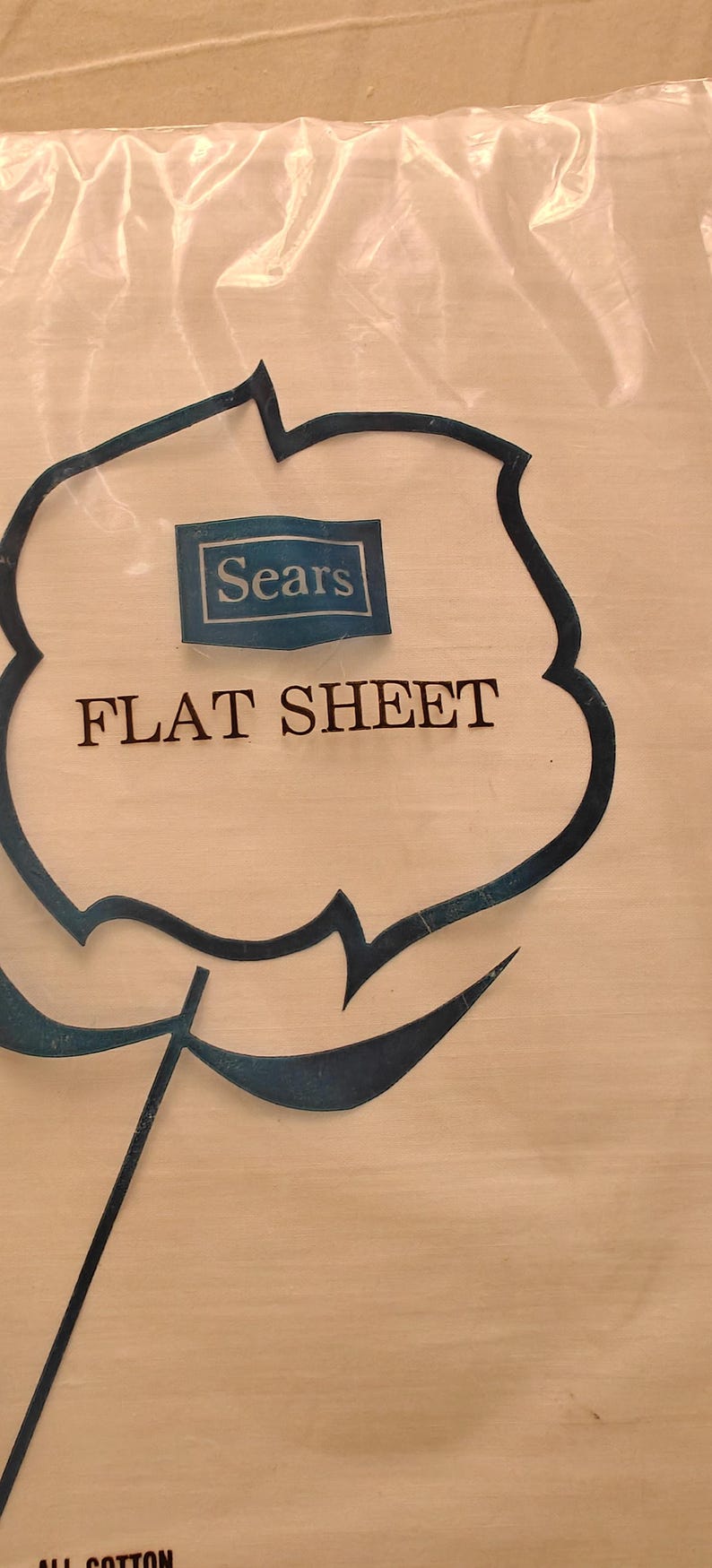 K&ouml;nnte beinhalten: Ein flaches Bettlaken in einer transparenten Plastikverpackung. Die Verpackung zeigt ein blau-wei&szlig;es Sears-Logo und die Worte "FLAT SHEET" in schwarzer Schrift. Das Laken scheint eine helle Farbe zu haben.