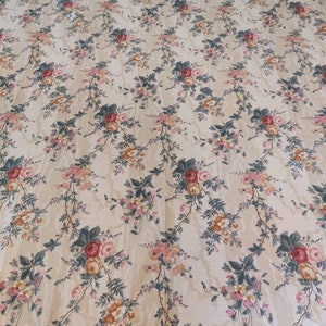 May include: Cream-colored floral bedspread with a repeating pattern of pink, red, and orange roses, green leaves, and delicate vines. The fabric has a subtle sheen, and the top edge is trimmed with a ruffled border.