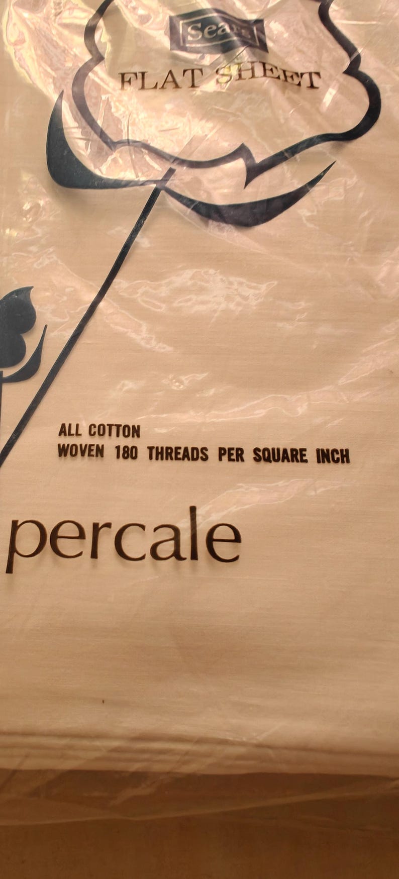K&ouml;nnte beinhalten: Verpackung eines flachen Bettlakens aus Baumwoll-Perkal. Die transparente Verpackung zeigt die Aufschrift &bdquo;FLAT SHEET&ldquo; und &bdquo;percale&ldquo;. Das Laken ist mit 180 F&auml;den pro Quadratzoll gewebt.