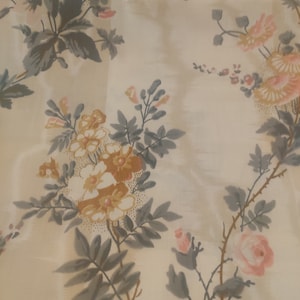 May include: A fabric featuring a cream-colored background with a repeating floral pattern. The design includes clusters of flowers in shades of soft pink, muted yellow, and white, accented by grey-green leaves and stems on thin brown vines.
