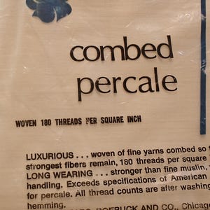 K&ouml;nnte beinhalten: Verpackung f&uuml;r gek&auml;mmten Percale-Stoff mit dem Text "gewebt 180 F&auml;den pro Quadratzoll". Das Design umfasst ein blaues Blumenmuster und den Text "Luxuri&ouml;s..." und "Langlebig..."