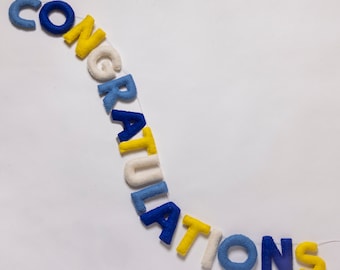May include: A felt banner with the word "CONGRATULATIONS" spelled out in blue, yellow and white letters. The letters are strung together with white thread.