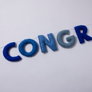 K&ouml;nnte beinhalten: Ein Filzbanner, das das Wort "CONGR" in Blaut&ouml;nen buchstabiert, von Dunkelblau bis Hellblau.
