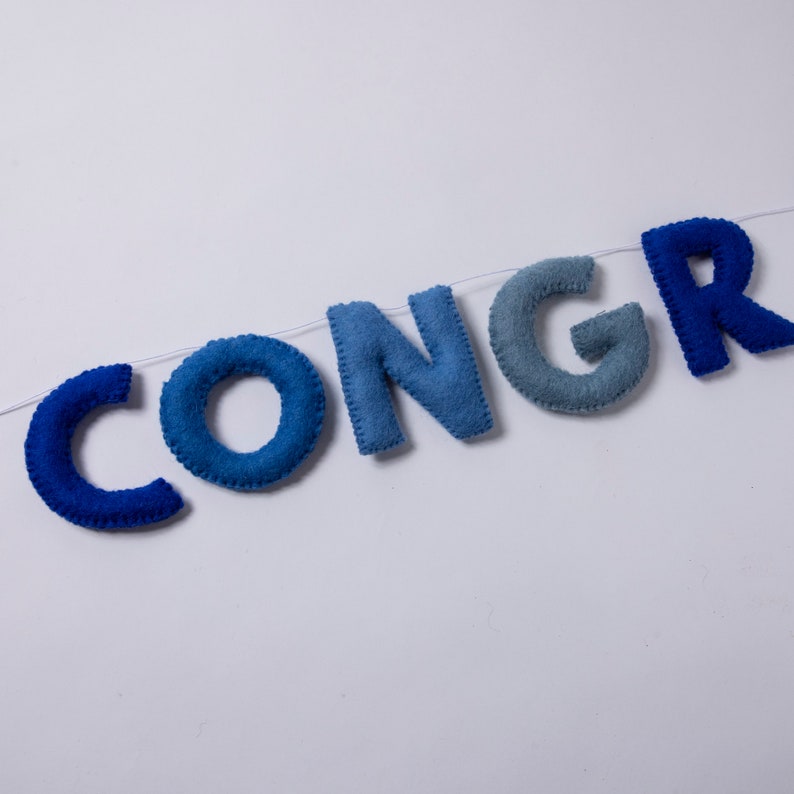 K&ouml;nnte beinhalten: Ein Filzbanner, das das Wort "CONGR" in Blaut&ouml;nen buchstabiert, von Dunkelblau bis Hellblau.