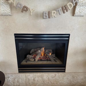 May include: A fireplace with a lit fire and a felt banner that reads "Happy Birthday" hanging above it.