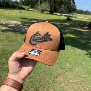 May include: A brown and black baseball cap with a black leather patch that says "Chevrolet" in a stylised font.