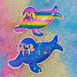 May include: Two holographic stickers of walruses with toothy grins. One walrus is rainbow colored with stars and a comet. The other walrus is blue with a crystal-like pattern.