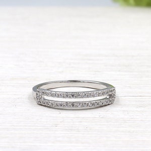 Pode incluir: Um anel de prata com duas fileiras de pequenas pedras transparentes. O anel &eacute; projetado para ser usado como uma alian&ccedil;a de casamento ou um anel de promessa.