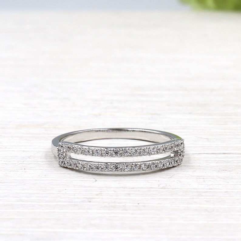 Pode incluir: Um anel de prata com duas fileiras de pequenas pedras transparentes. O anel &eacute; projetado para ser usado como uma alian&ccedil;a de casamento ou um anel de promessa.
