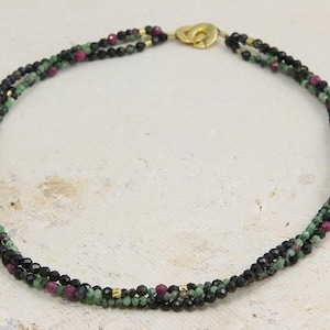 Könnte beinhalten: Eine mehrreihige Halskette mit schwarzen, grünen und rosafarbenen Perlen. Die Halskette besteht aus kleinen, runden Perlen und hat einen goldenen Verschluss.