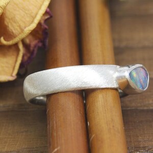 May include: A silver band ring with a brushed finish and a single iridescent opal gemstone set in the band.