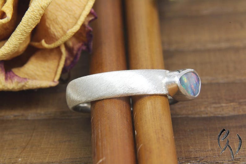May include: A silver band ring with a brushed finish and a single iridescent opal gemstone set in the band.