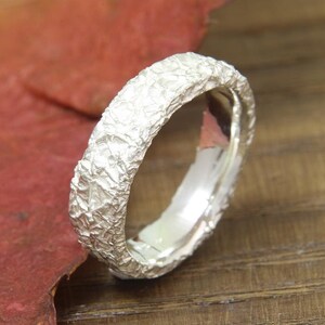 May include: A silver ring with a textured, rough surface. The ring is a simple band with a hammered finish.