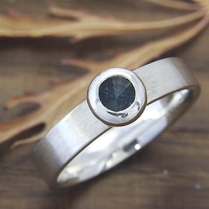 May include: A silver ring with a bezel setting featuring a dark blue gemstone.