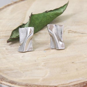 May include: A pair of silver earrings with a twisted, abstract design. The earrings are displayed on a wooden surface.