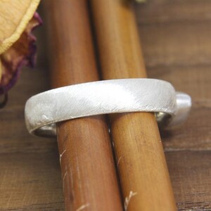 May include: A silver ring with a brushed finish. The ring is sitting on two wooden dowels.