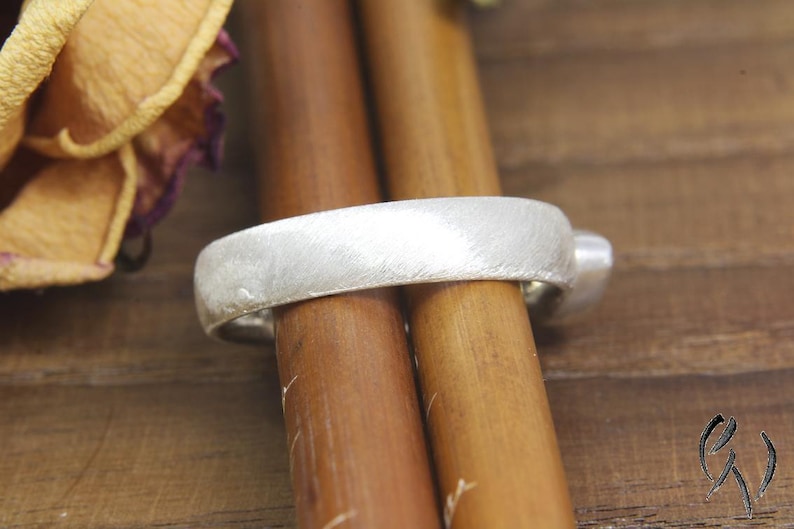 May include: A silver ring with a brushed finish. The ring is sitting on two wooden dowels.