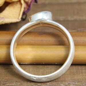 May include: A silver ring with a textured finish. The ring is oval shaped and has a smooth, rounded edge.
