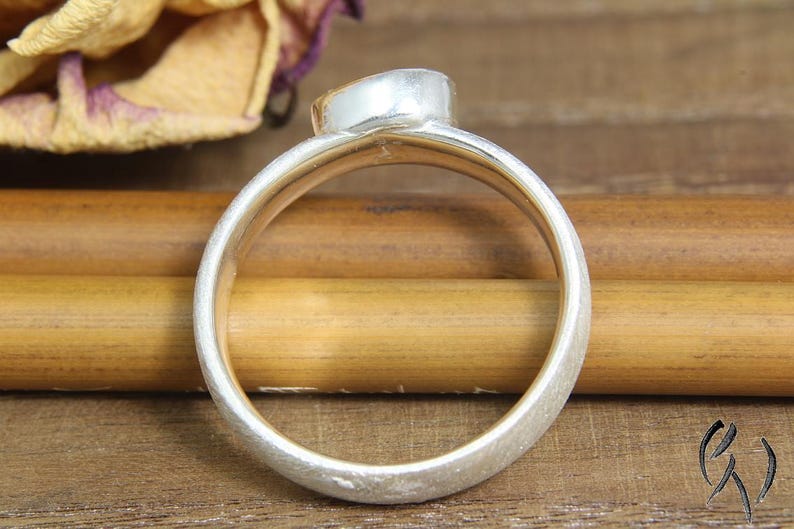May include: A silver ring with a textured finish. The ring is oval shaped and has a smooth, rounded edge.
