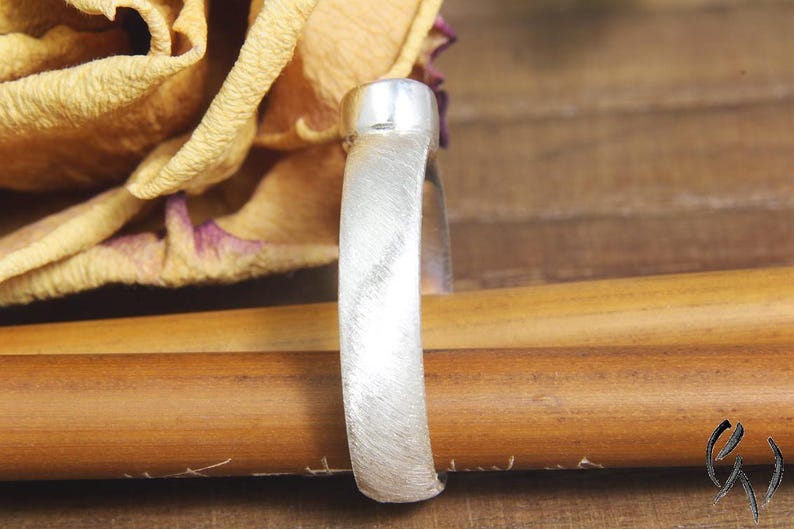 May include: A silver ring with a brushed finish. The ring is on a wooden surface.