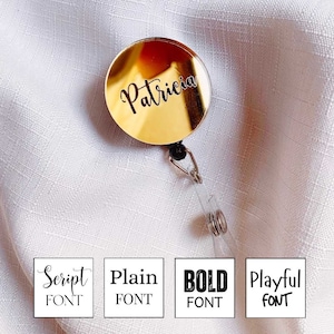 May include: Gold retractable badge holder with the name "Patricia" engraved in a script font.  The holder is shown against a white fabric background.  Four font options are shown below the holder: Script, Plain, Bold, and Playful.