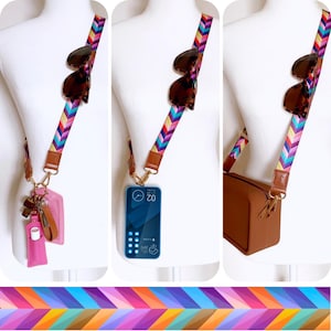 May include: A multi-coloured chevron patterned crossbody strap with brown leather accents. The strap is shown with sunglasses, a phone, a small brown purse, and a pink cardholder with keys and a lip balm.