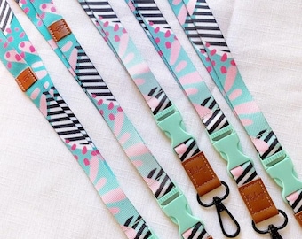 May include: Four colorful patterned lanyards with black and white stripes and pink and green accents. Each lanyard has a plastic clip and a brown leather tag with the word "Hello" printed on it.
