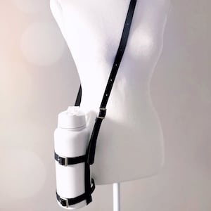May include: A white water bottle with a black strap and buckles. The strap is adjustable and can be worn over the shoulder.