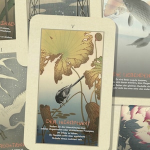 May include: A set of tarot cards with Japanese-inspired artwork. The cards feature images of birds, flowers, and fish. The cards are in a variety of colors, including blue, green, and red. The text on the cards is in German.