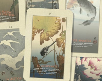May include: A set of tarot cards with Japanese-inspired artwork. The cards feature images of birds, flowers, and fish. The cards are in Spanish and have the names of the cards written on them. The cards are on a light brown surface.