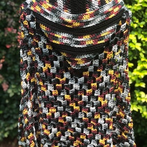 May include: A crocheted shawl with a hood in black, gray, burgundy, and gold colors. The shawl has a lacy pattern and is made with a soft yarn.