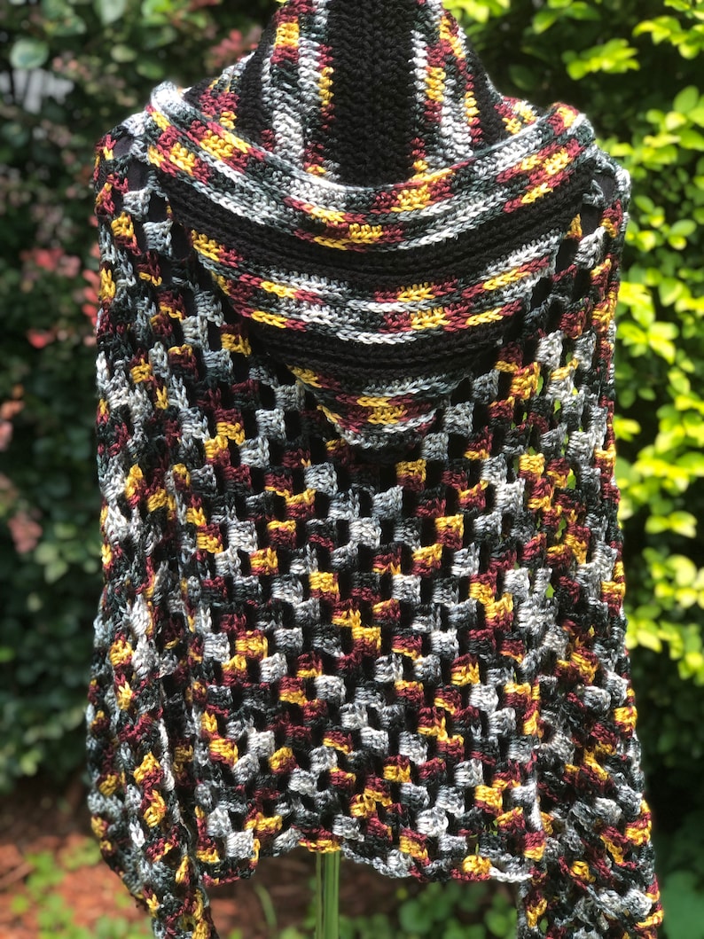 May include: A crocheted shawl with a hood in black, gray, burgundy, and gold colors. The shawl has a lacy pattern and is made with a soft yarn.