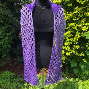 May include: A purple and lavender ombre crochet scarf with a hood. The scarf is displayed on a black mannequin.