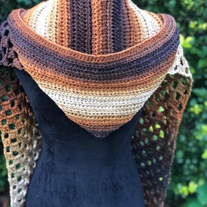 May include: A crocheted shawl with a hooded design in brown, beige, and tan colors. The shawl is made with a lacy stitch pattern and has a striped pattern on the hood.