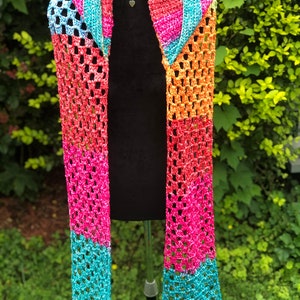 May include: A colorful crocheted scarf with a rainbow pattern. The scarf is made with a sparkly yarn and has a fringed edge.