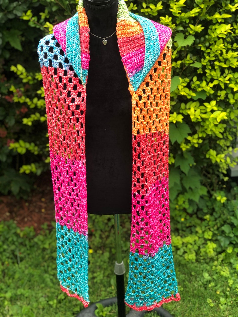 May include: A colorful crocheted scarf with a rainbow pattern. The scarf is made with a sparkly yarn and has a fringed edge.