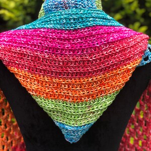 May include: A colorful crocheted triangular scarf with a rainbow pattern. The scarf is made with a variety of shades of blue, green, orange, pink, and red yarn.