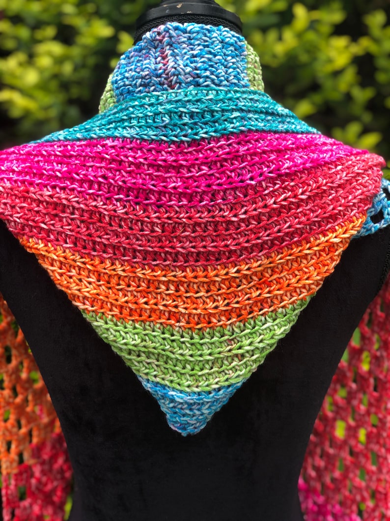 May include: A colorful crocheted triangular scarf with a rainbow pattern. The scarf is made with a variety of shades of blue, green, orange, pink, and red yarn.