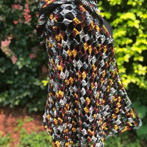 May include: A crocheted shawl with a black, burgundy, gold, and silver color pattern. The shawl is made with a loose, open stitch and has a fringed edge.