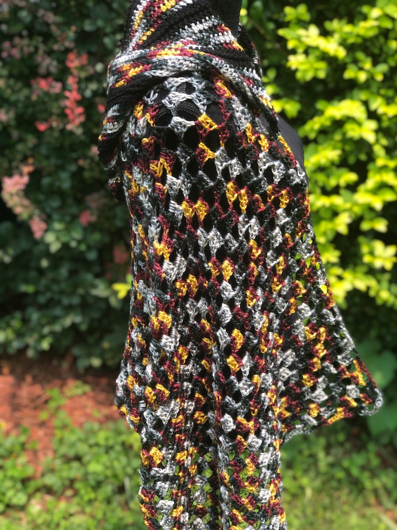 May include: A crocheted shawl with a black, burgundy, gold, and silver color pattern. The shawl is made with a loose, open stitch and has a fringed edge.