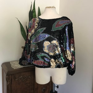 May include: A black sequined top with a floral pattern in shades of gold, green, blue, and red.