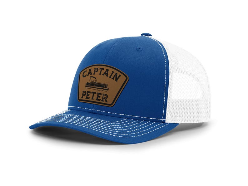 May include: A blue and white trucker hat with a curved brim. The front panel is blue, and the back is white mesh. A brown patch with the words "CAPTAIN PETER" and a boat graphic is on the front.
