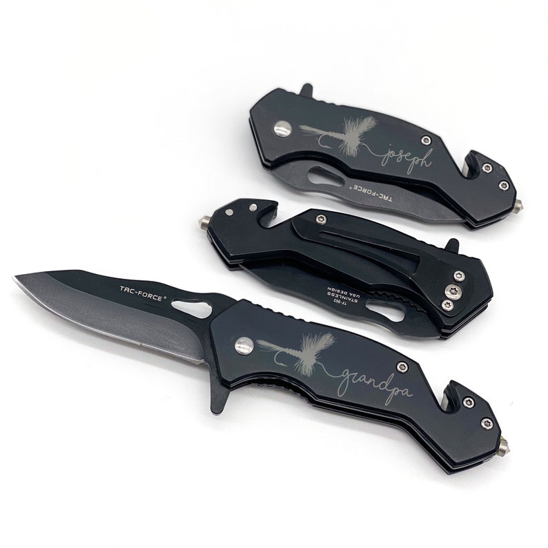 May include: Three black pocket knives with a fly fishing lure design and personalized names. The knives have a black handle and a silver blade. The names are "Joseph", "Grandpa", and "TAC-FORCE".