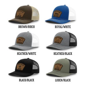 May include: A collection of six trucker hats in various colors, each featuring a patch with the word "CAPTAIN" or "FIRST MATE" and a name. Colors include brown, blue, gray, black, and green. The hats have mesh backs and curved visors.