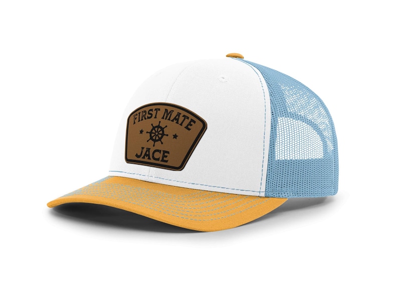May include: A trucker hat with a white front panel, a light blue mesh back, and a yellow brim. The hat features a brown patch with the words "FIRST MATE JACE" and a ship's wheel design.