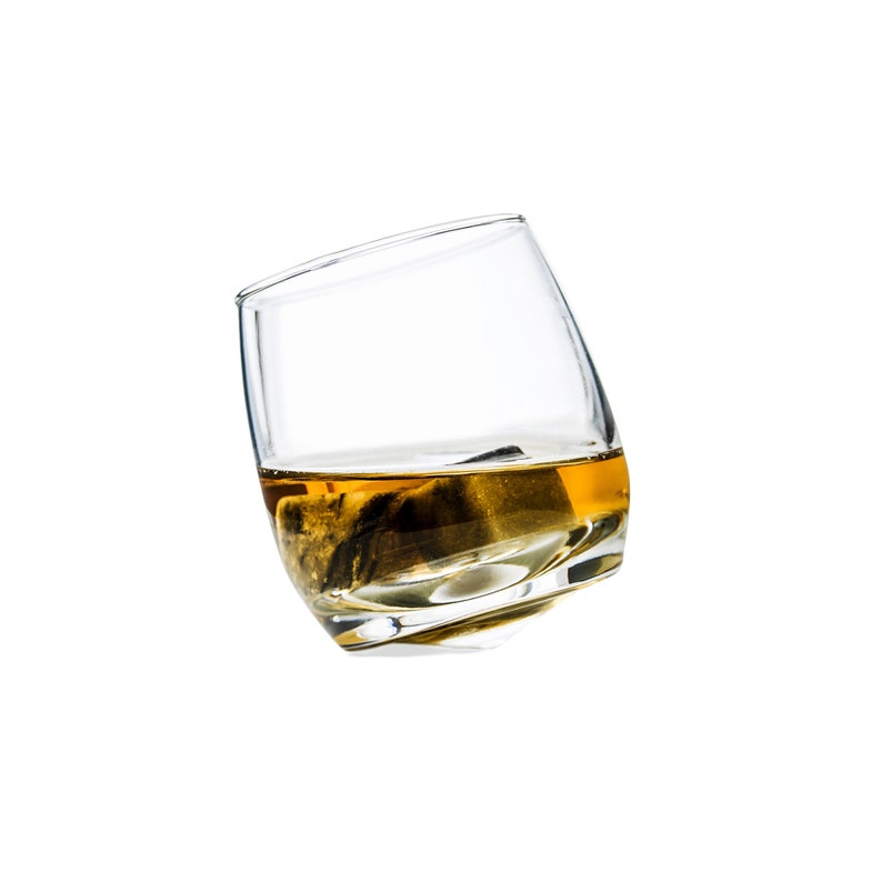 May include: A clear glass with a rounded bottom filled with a golden liquid and a dark ice cube.