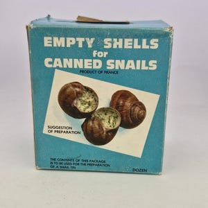 May include: A blue box with the text "EMPTY SHELLS for CANNED SNAILS PRODUCT OF FRANCE" and a picture of three empty snail shells. The text "SUGGESTION OF PREPARATION" and "THE CONTENTS OF THIS PACKAGE IS TO BE USED FOR THE PREPARATION OF A SNAIL TIN DOZEN" is also on the box.
