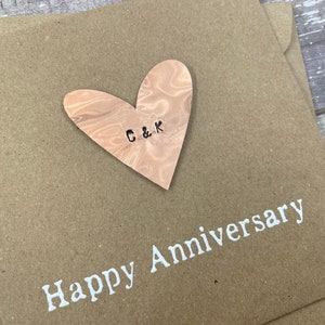 Puede incluir: Una tarjeta marr&oacute;n con un coraz&oacute;n de madera pegado. El coraz&oacute;n tiene las iniciales "C & K" talladas en &eacute;l. La tarjeta dice "Feliz Aniversario" en letras blancas.