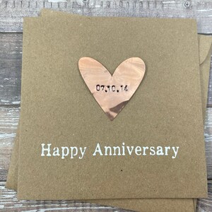 Puede incluir: Una tarjeta marr&oacute;n con un recorte en forma de coraz&oacute;n blanco con la fecha "07.10.14" grabada en ella. La tarjeta dice "Feliz Aniversario" en texto blanco.